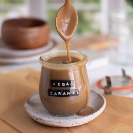 Jar of homemade vegan caramel with a spoon dripping caramel sauce.