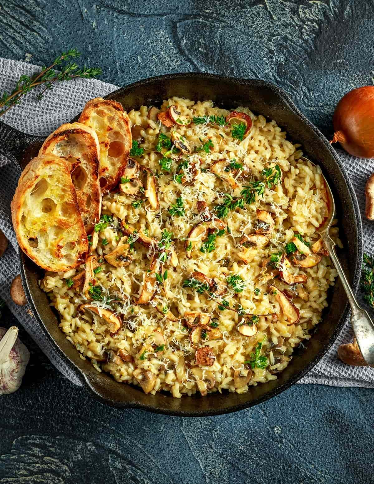 A cast iron skillet full of vegan garlic oyster mushroom risotto with two slices of toasted bread.