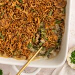 Vegan green bean casserole with crispy onions on top and a spoon scooping out a serving.