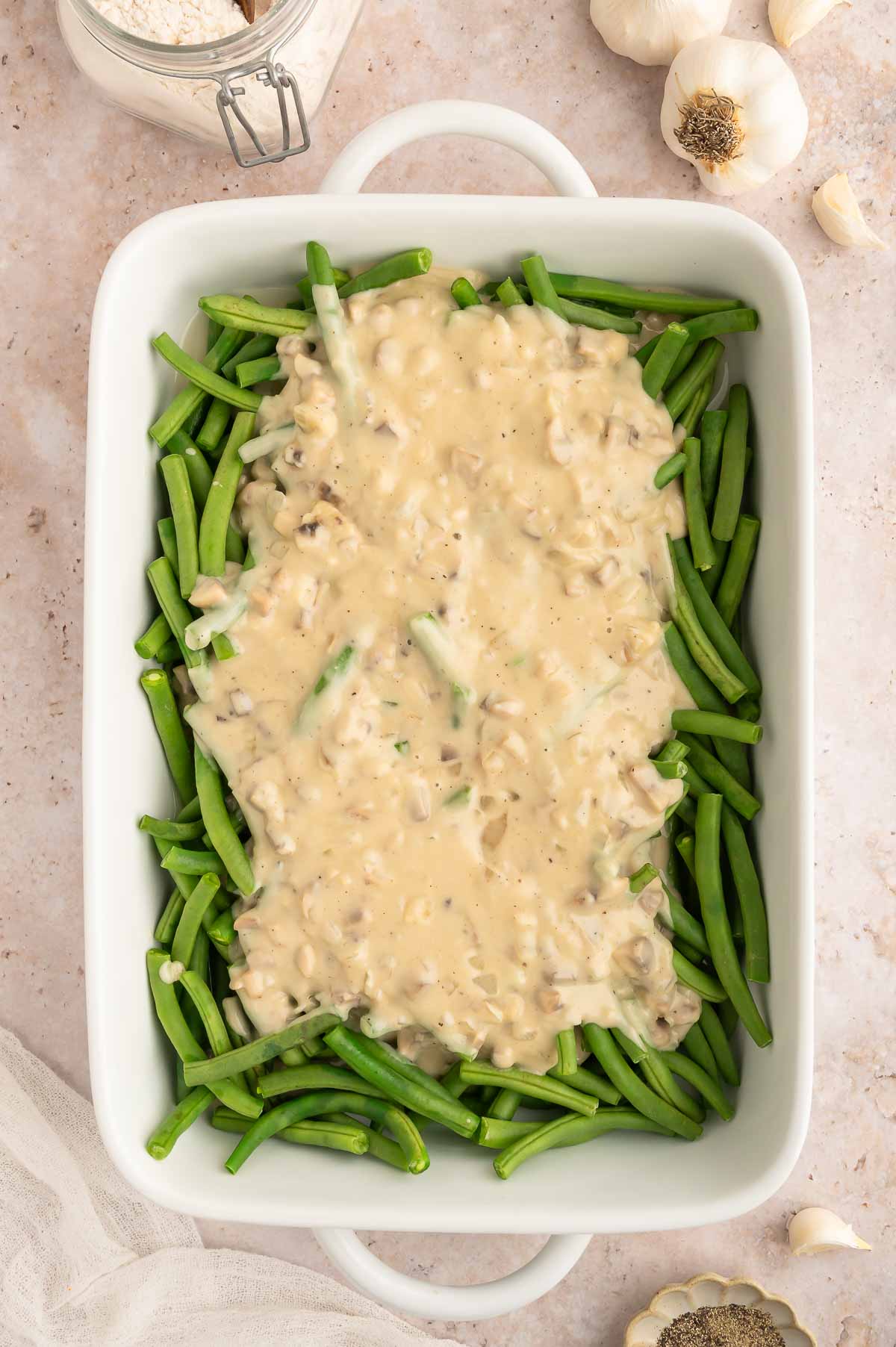 The steamed green beans added to a casserole dish and topped with a creamy mushroom sauce.