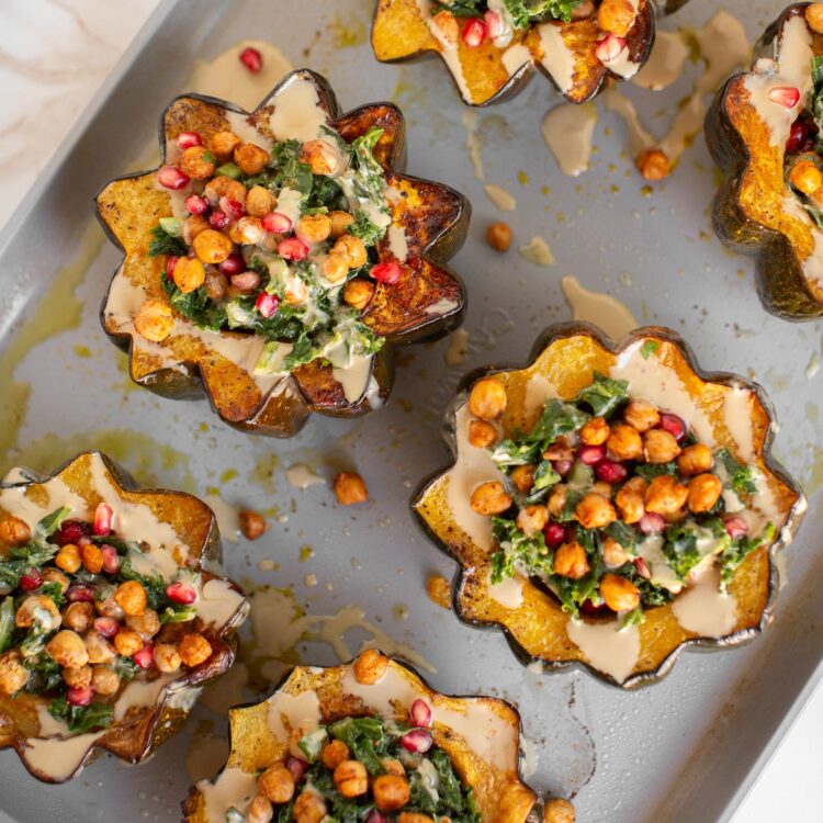 Delicious vegan holiday recipe for acorn squash roasted on a baking sheet and topped with kale, chickpeas, and tahini.