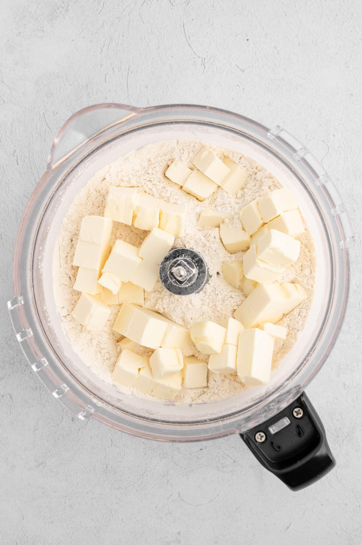 Cubed vegan butter added on top of the flour mixture in a food processor.