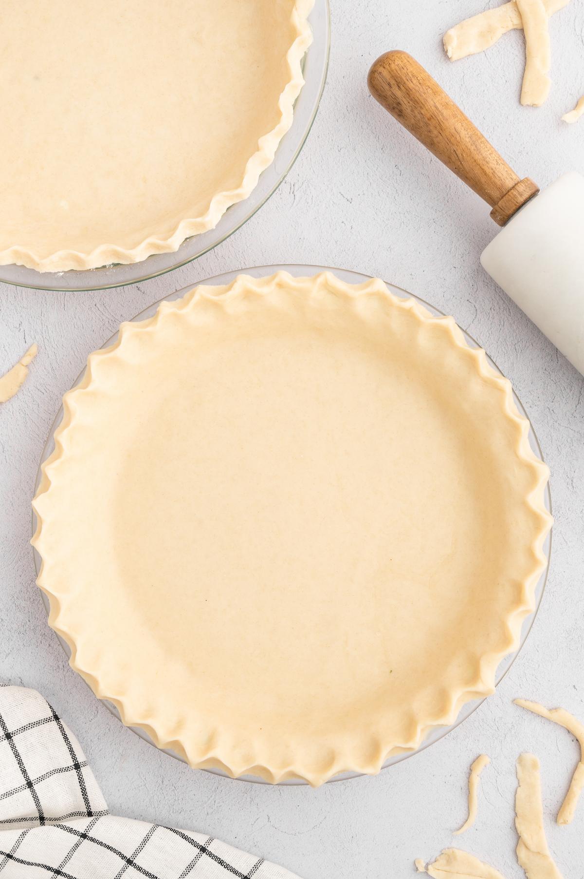 Two vegan pie crusts in pie pans next to a rolling pin.