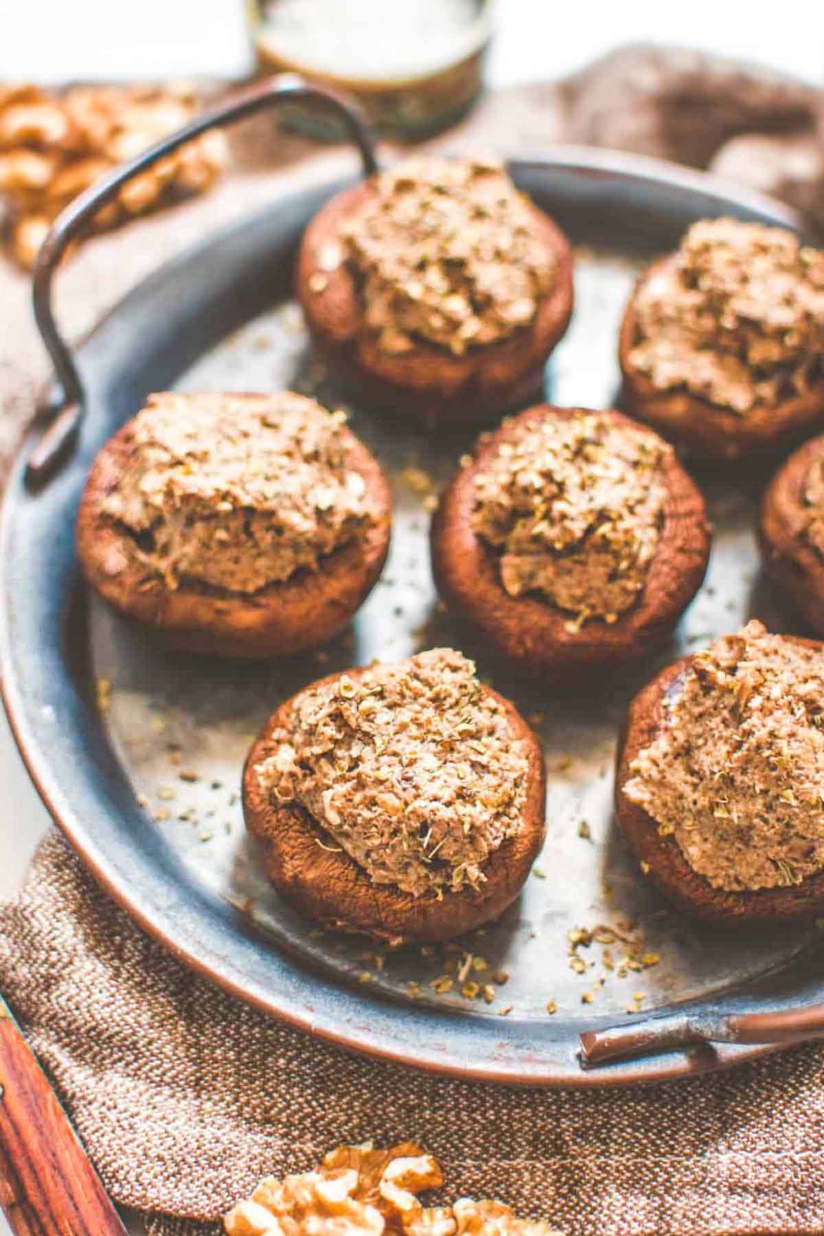 Warm, oven-roasted mushrooms filled with a rich, herby walnut mixture, served on a vintage tray with a knife and rustic napkin.
