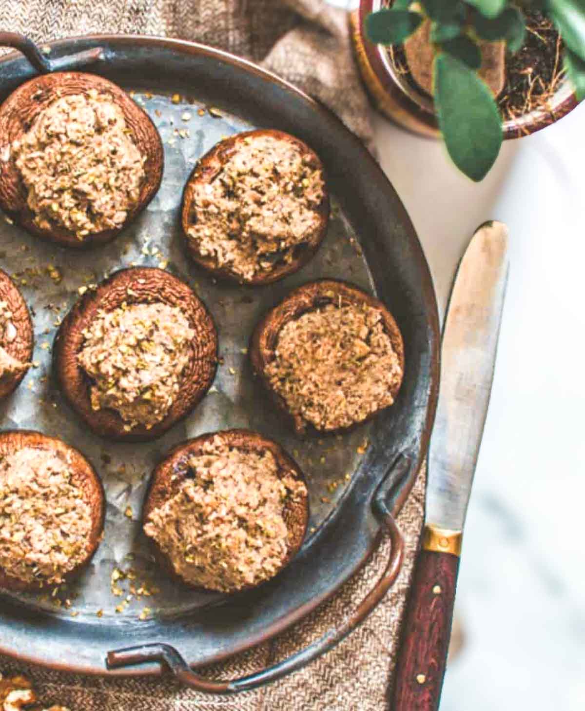A rustic serving tray with golden-baked mushrooms, generously stuffed with a creamy walnut filling and sprinkled with herbs.