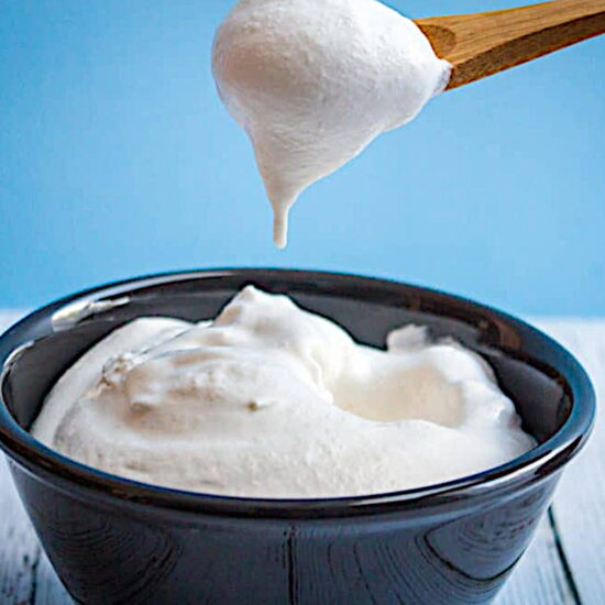A spoon scooping up a dollop of coconut whipped cream from a bowl.