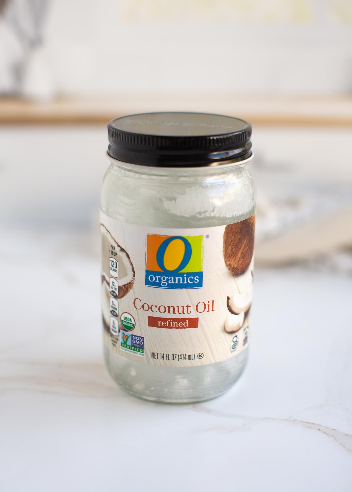 Glass jar of organic refined coconut oil on a table.