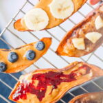 Slices of sweet potato toast on a cooling rack, topped with nut butters, berries, and jam.