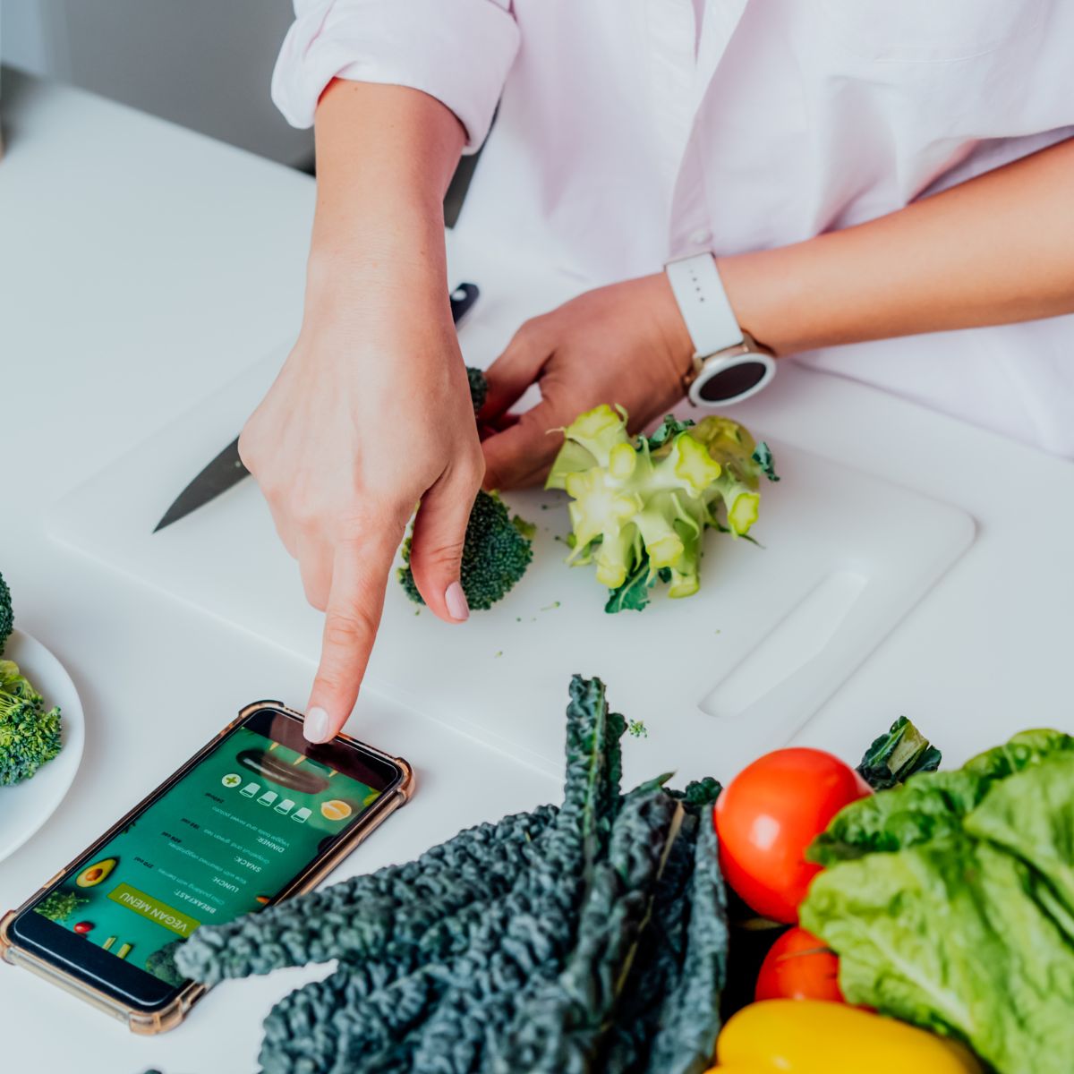 A woman using her phone on a counter, surrounded by produce.