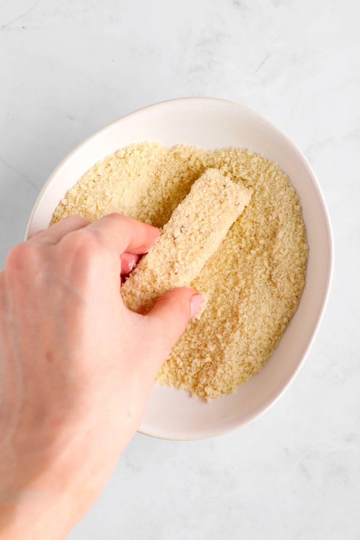 A hand dipping the wet cornstarch-coated tofu slice in a bowl of Panko bread crumbs.