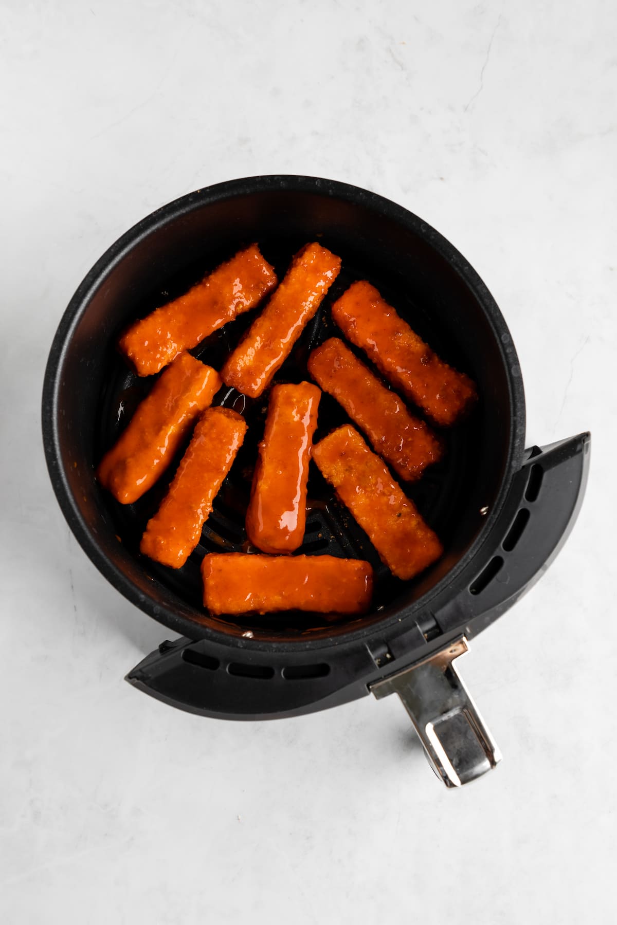 Tofu wings coated in buffalo sauce in an air fryer basket.