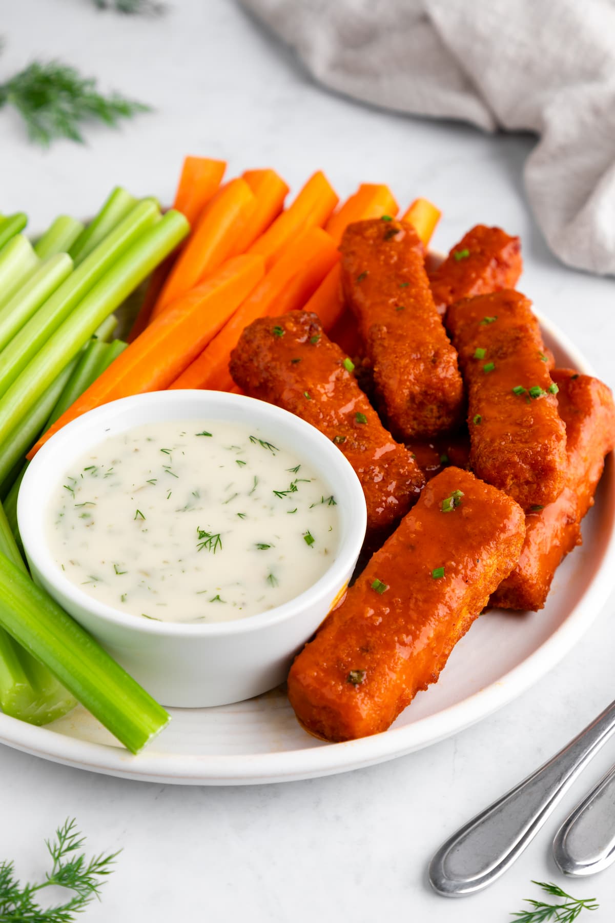 Vegan buffalo wings on a plate with vegan ranch and veggie sticks.