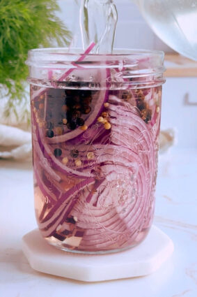 Pickling brine being poured into the jar of sliced red onions and spices.