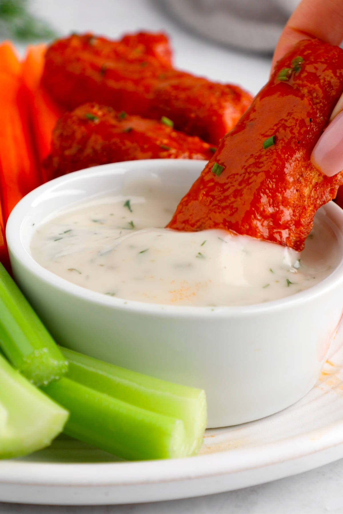 A buffalo tofu wing being dipped into a bowl of vegan ranch.