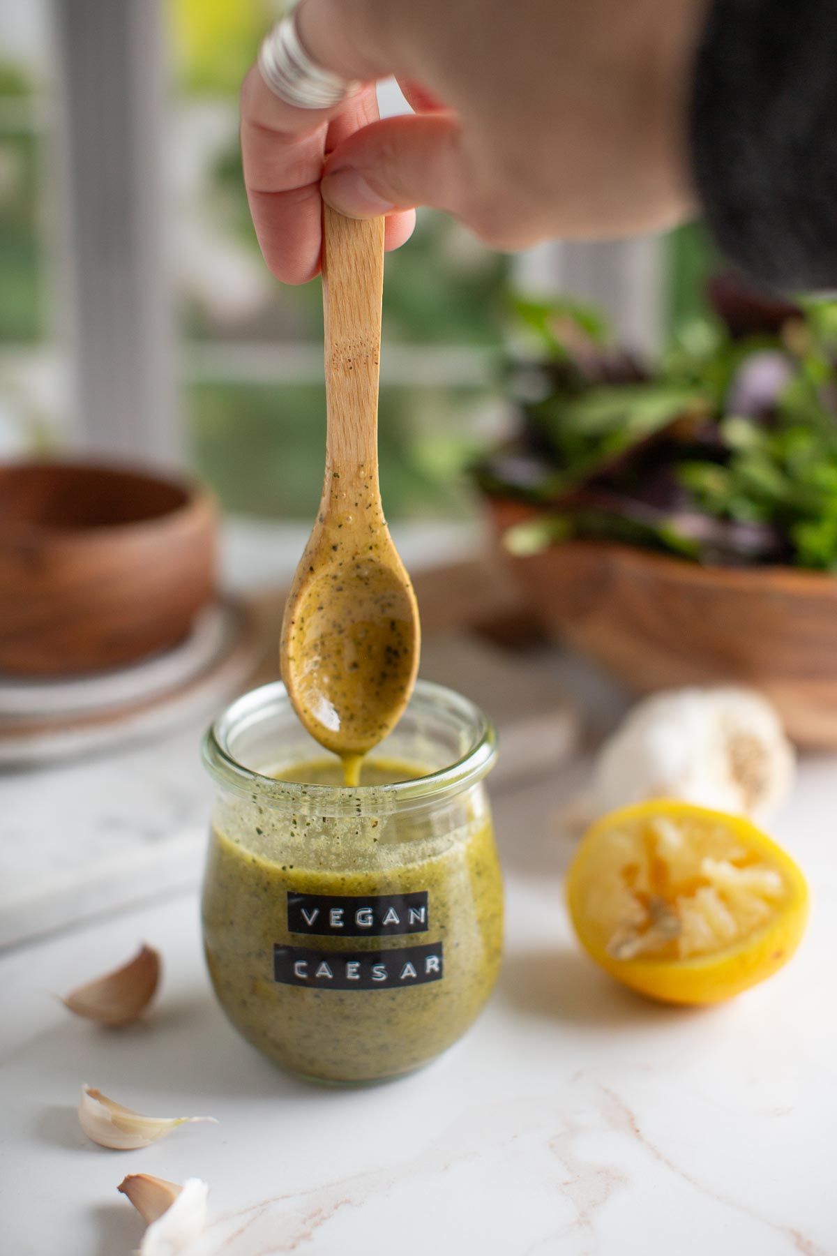 Jar of vegan caesar dressing served next to a salad with wooden bowls. 