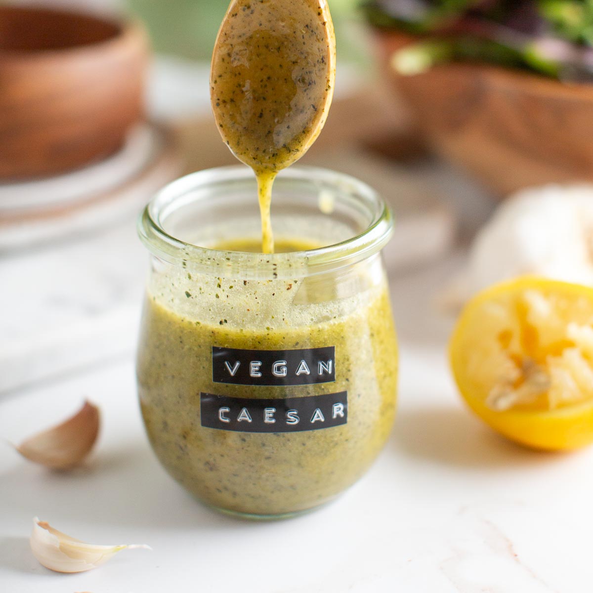 Glass jar with homemade vegan caesar dressing in it being drizzled with a wooden spoon.