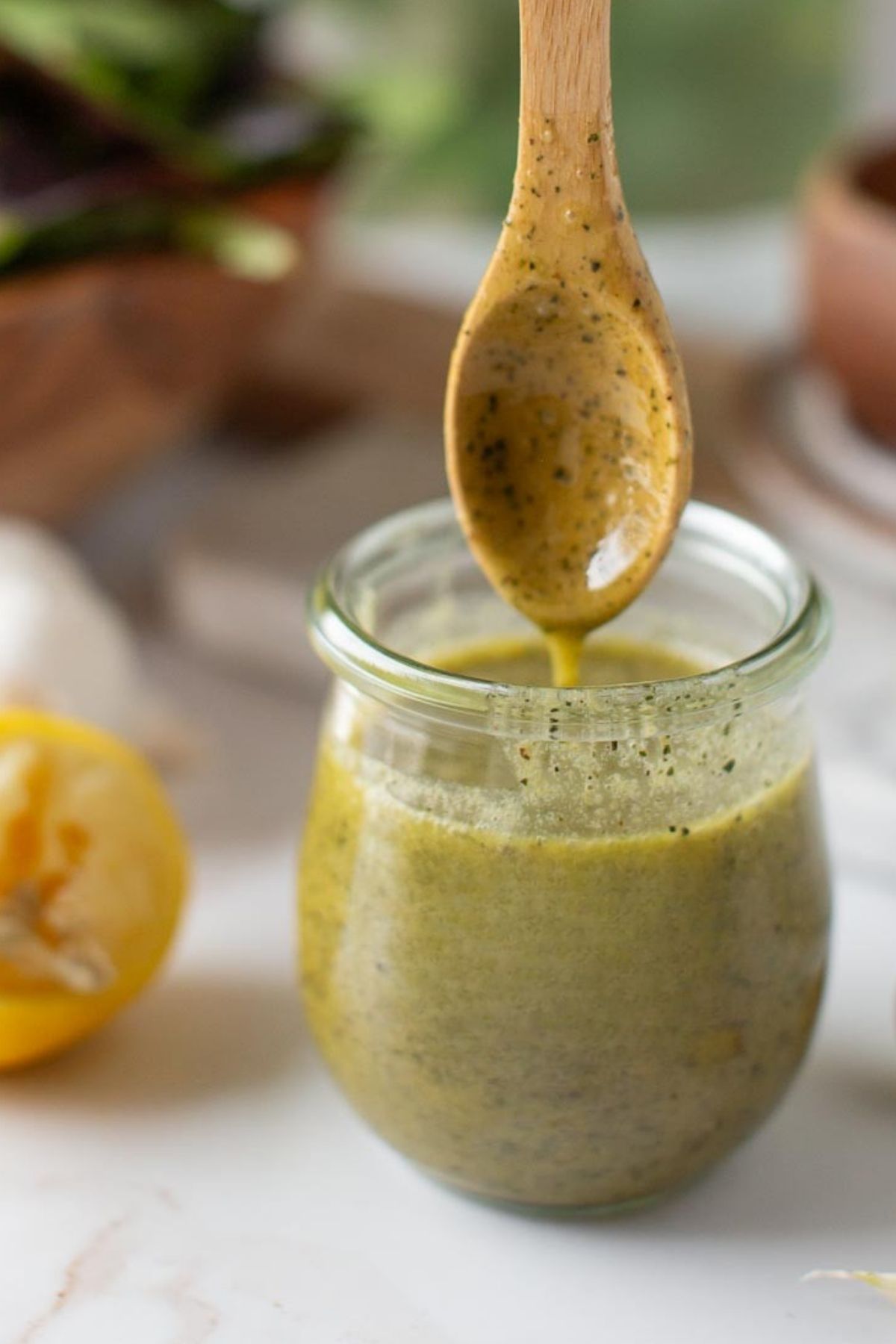 A spoon dipping into a jar of creamy vegan Caesar dressing, showing its thick and smooth texture.