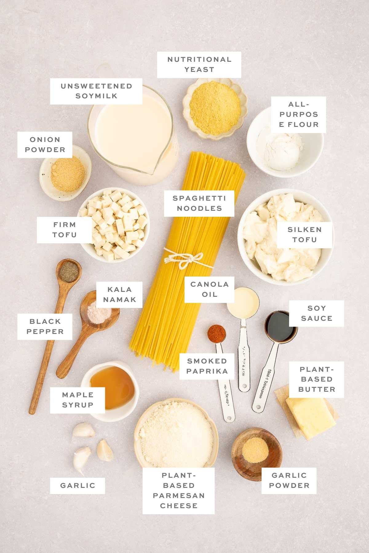 Flat lay of ingredients for vegan carbonara including tofu, pasta, plant-based milk, spices, and vegan cheese.