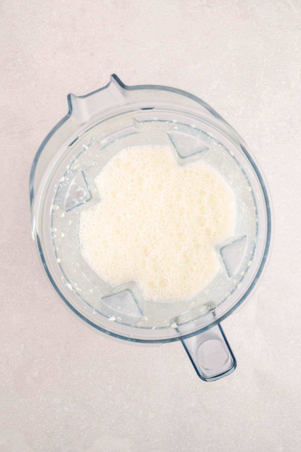 Blended silken tofu and soy milk base for vegan carbonara sauce inside a blender.