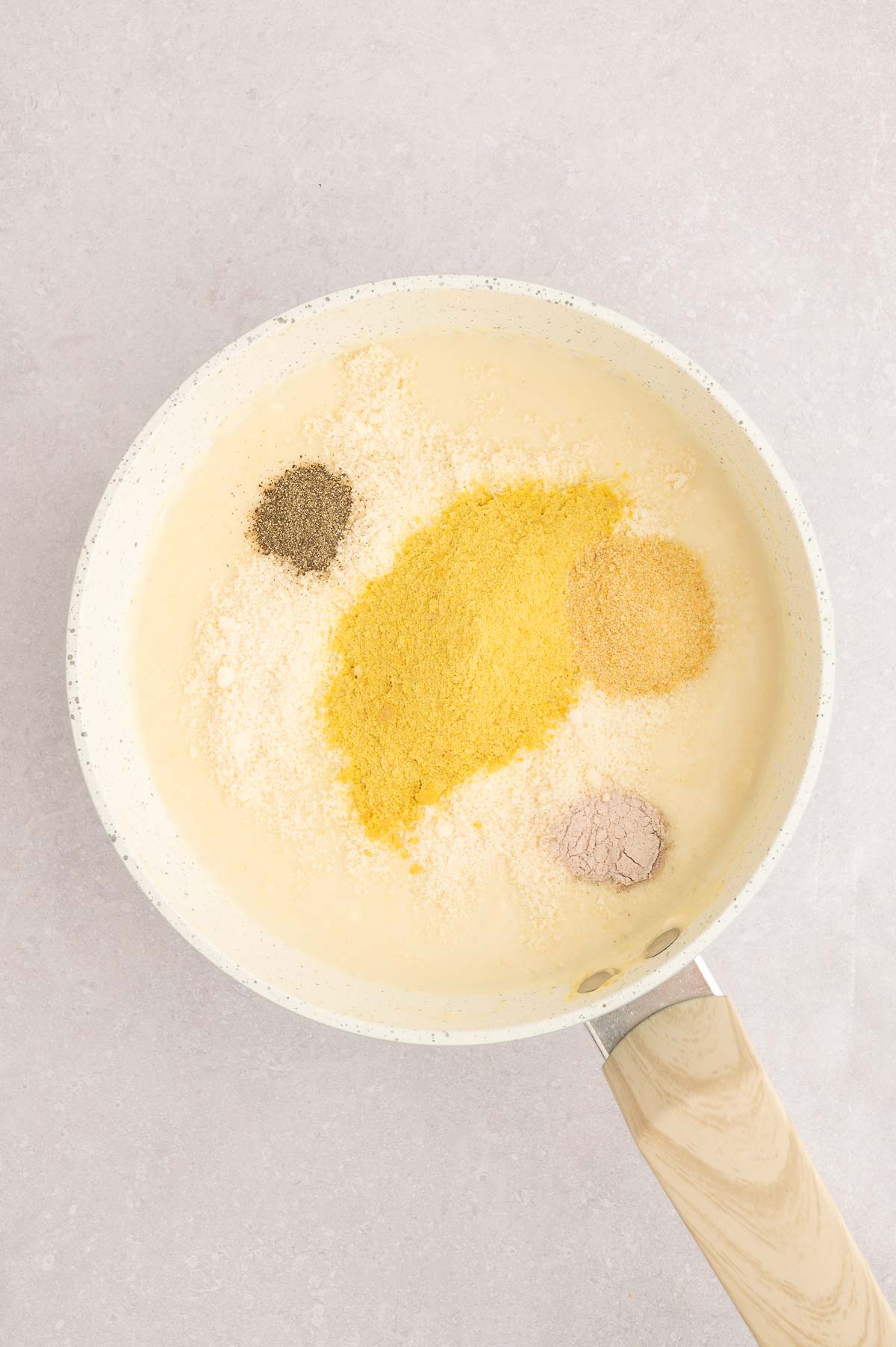 Seasonings added to vegan carbonara sauce including black salt, nutritional yeast, and vegan cheese.