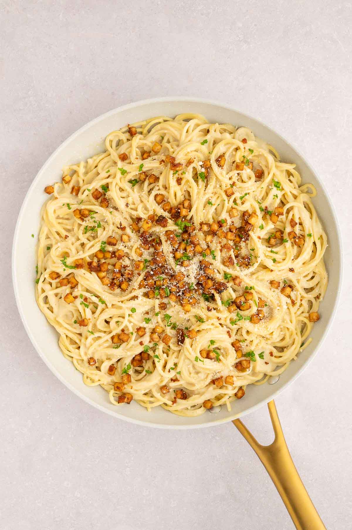 Pan of vegan carbonara with tofu bacon and chopped parsley ready to serve.