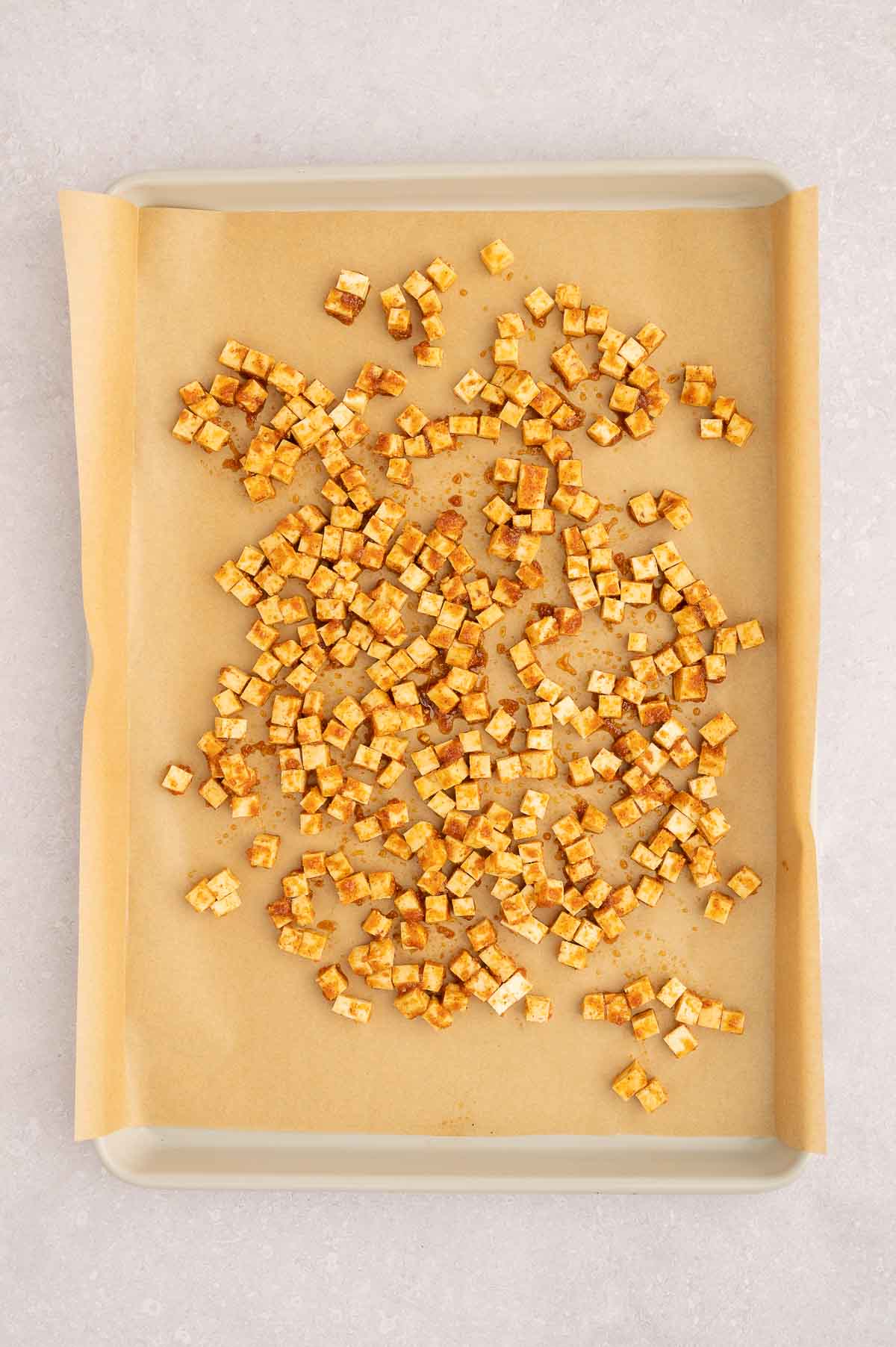 Diced tofu cubes marinated and spread on a parchment-lined tray for vegan carbonara topping.