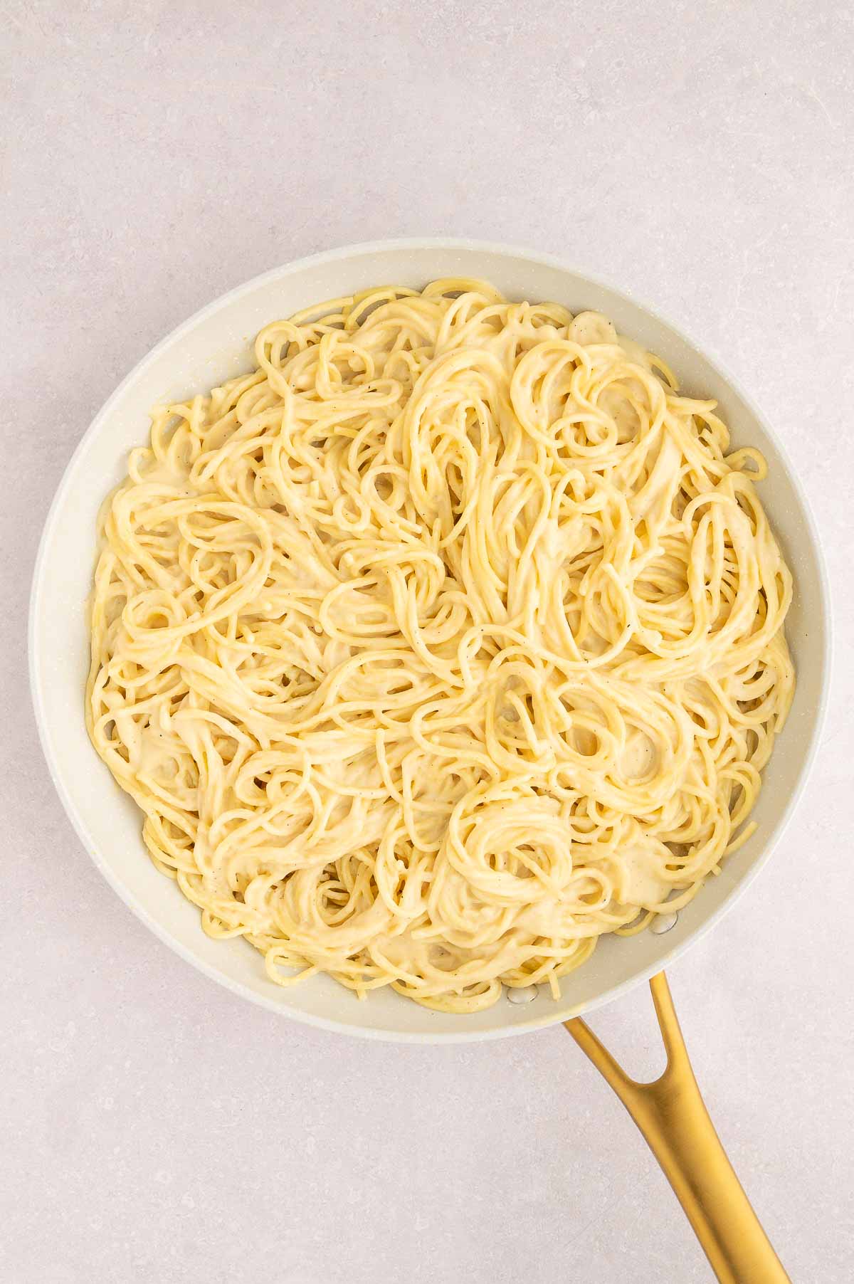 Vegan carbonara pasta tossed with creamy sauce and plant-based ingredients in a white pan.