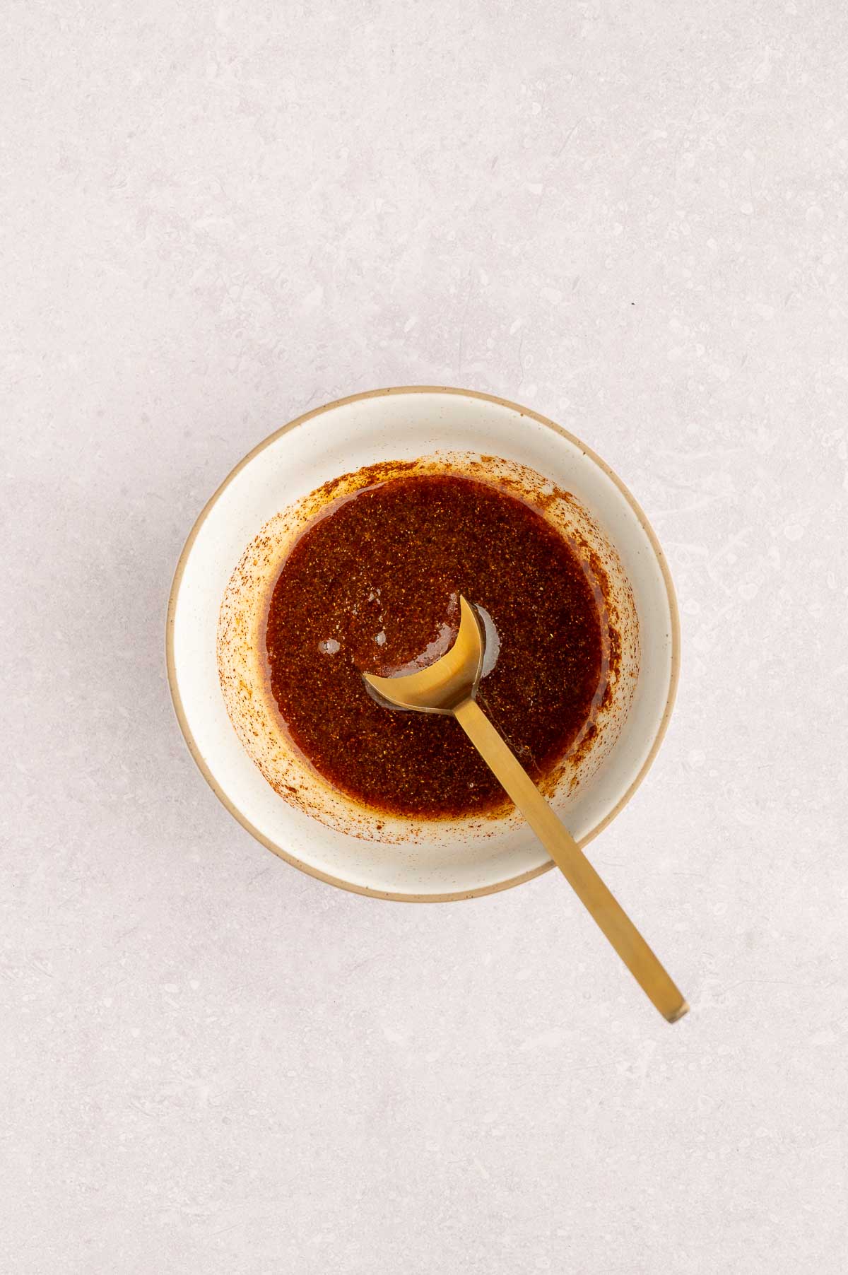 Whisked vegan bacon marinade in a bowl with golden spoon, ready to coat tofu for vegan carbonara.