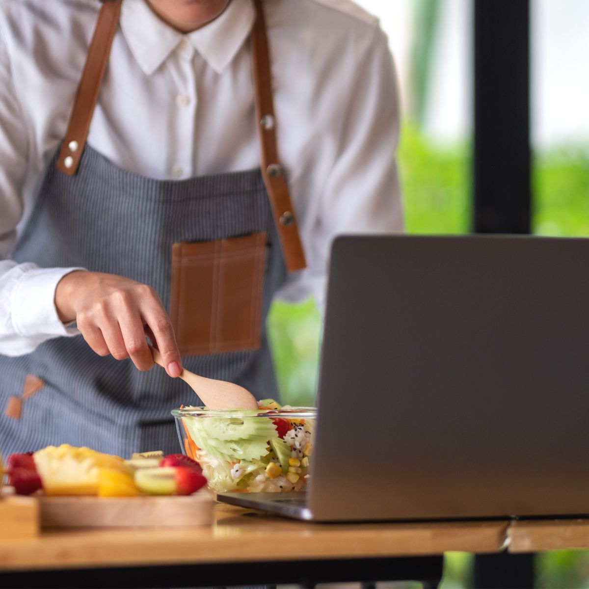 A student cooking in a kitchen with a laptop.