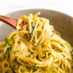 A wooden spoon lifts up a scoop of vegan one-pot pasta noodles.