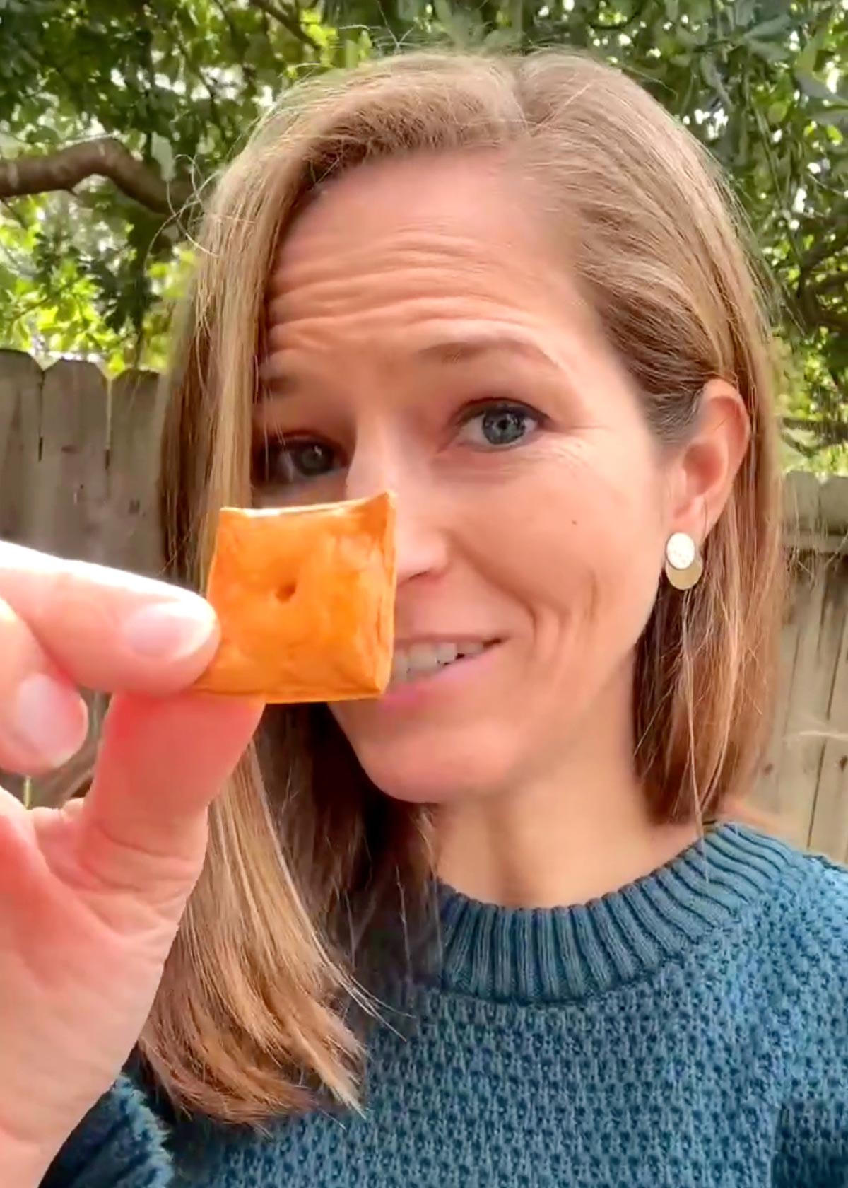 Michelle Cehn holding up a homemade orange vegan cheez it cracker. 