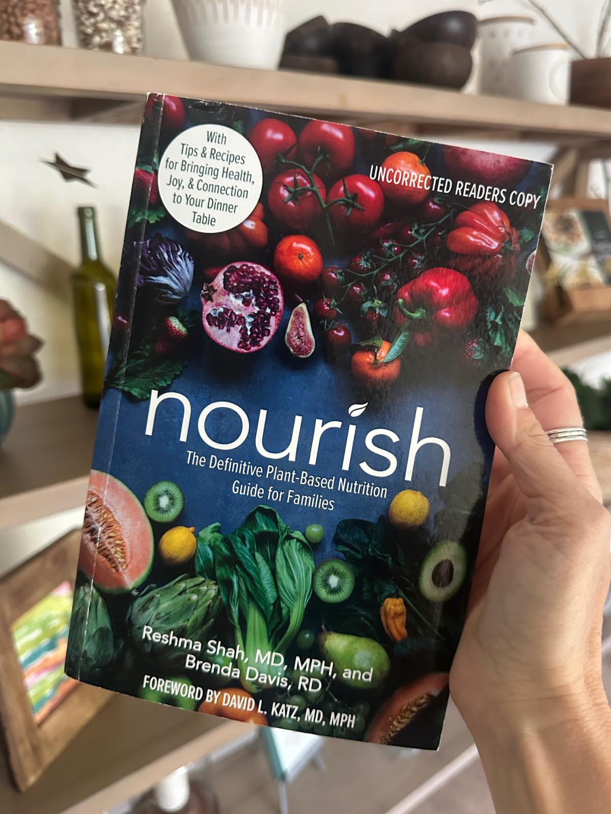 Holding a copy of the book Nourish by Dr. Reshma Shah, a plant-based diet book for families raising vegan children.