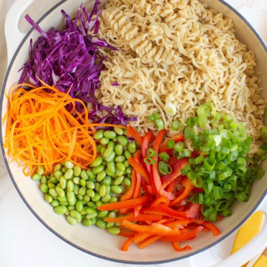A large serving bowl with peanut butter ramen noodle salad and colorful veggies.
