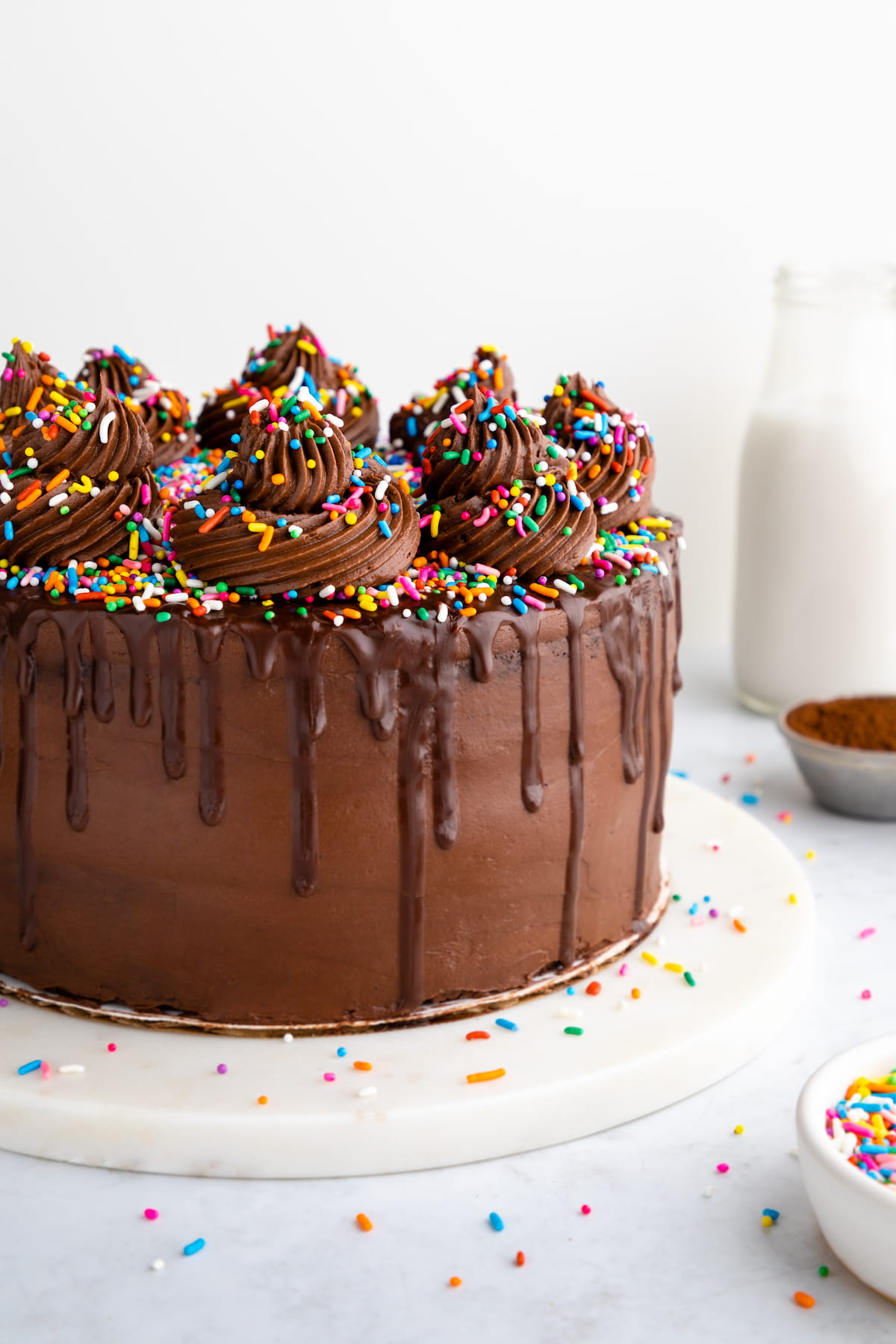 Vegan chocolate cake on a serving platter, topped with swirls of frosting and vegan sprinkles.