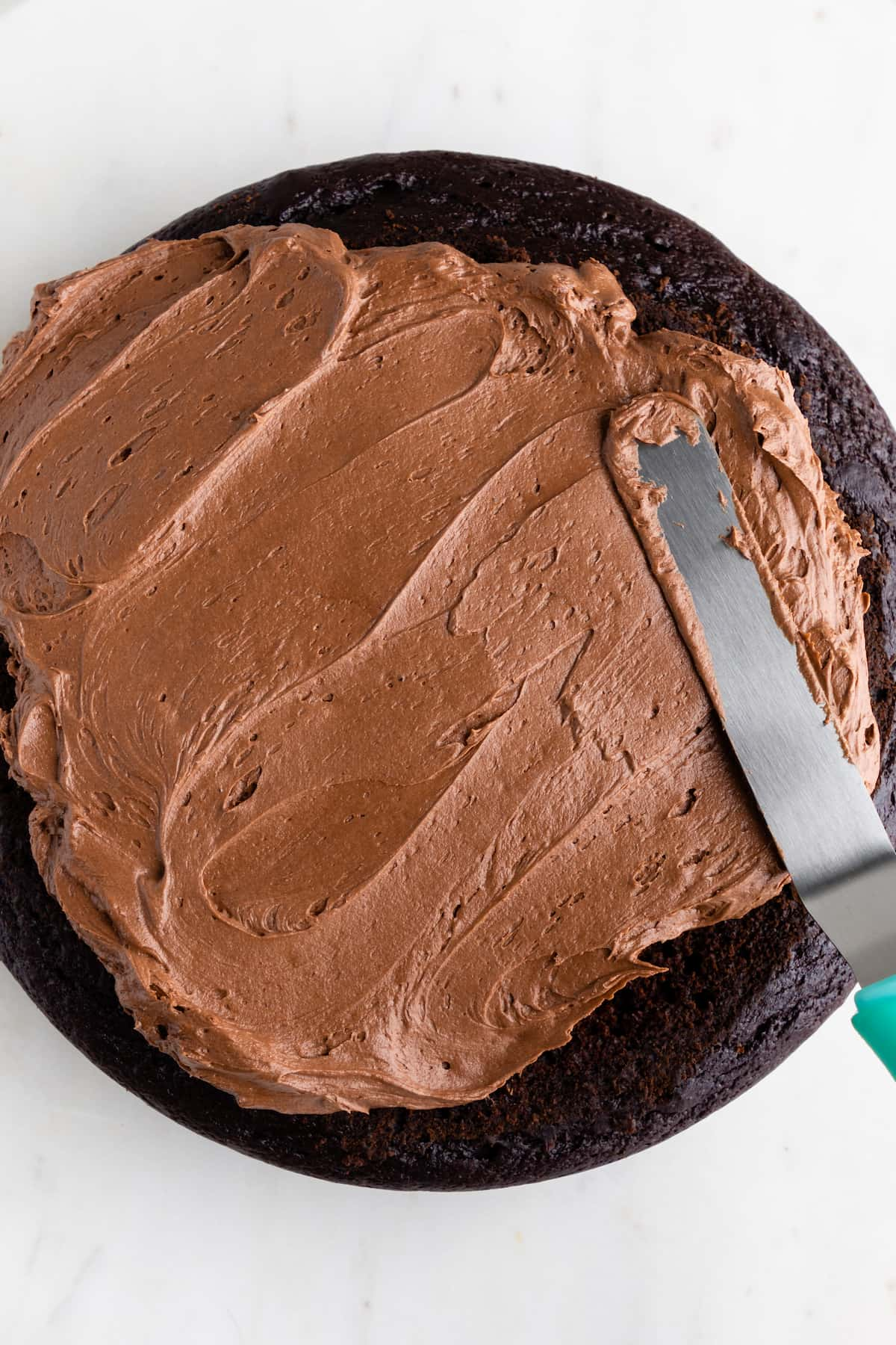 Vegan chocolate frosting being spread over a cake with an icing spatula.