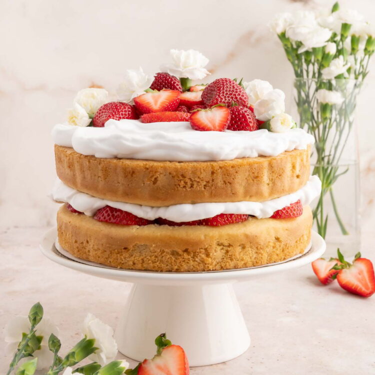 A two layer vegan strawberry shortcake cake topped with vegan whipped cream, fresh strawberries, and flowers.