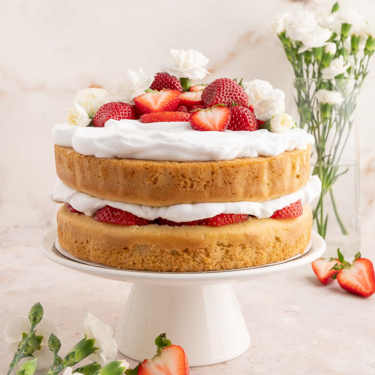 A two layer vegan strawberry shortcake cake topped with vegan whipped cream, fresh strawberries, and flowers.