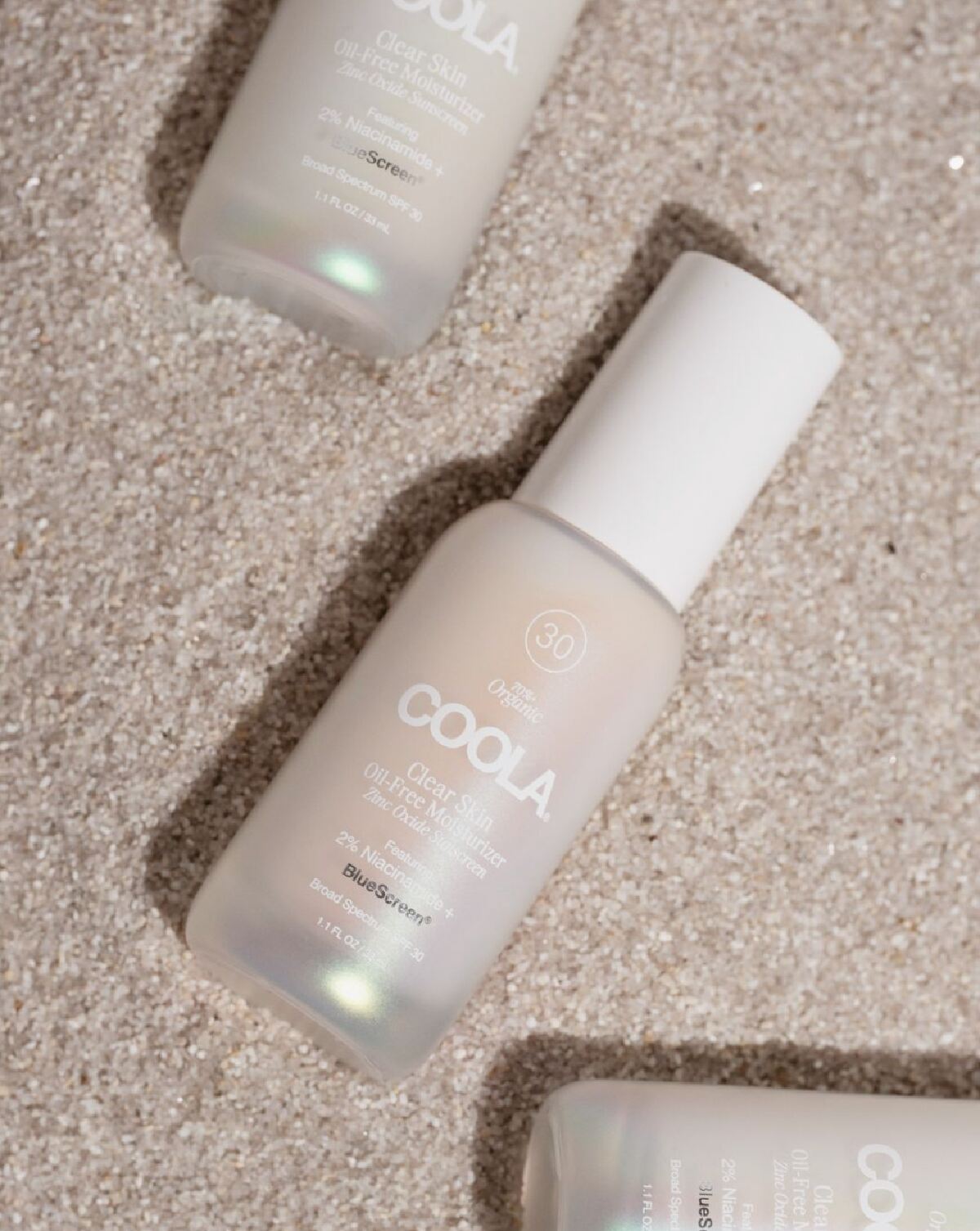 Coola's oil free moisturizer with SPF 30 in a clear bottle with white cap against a pink sandy background.