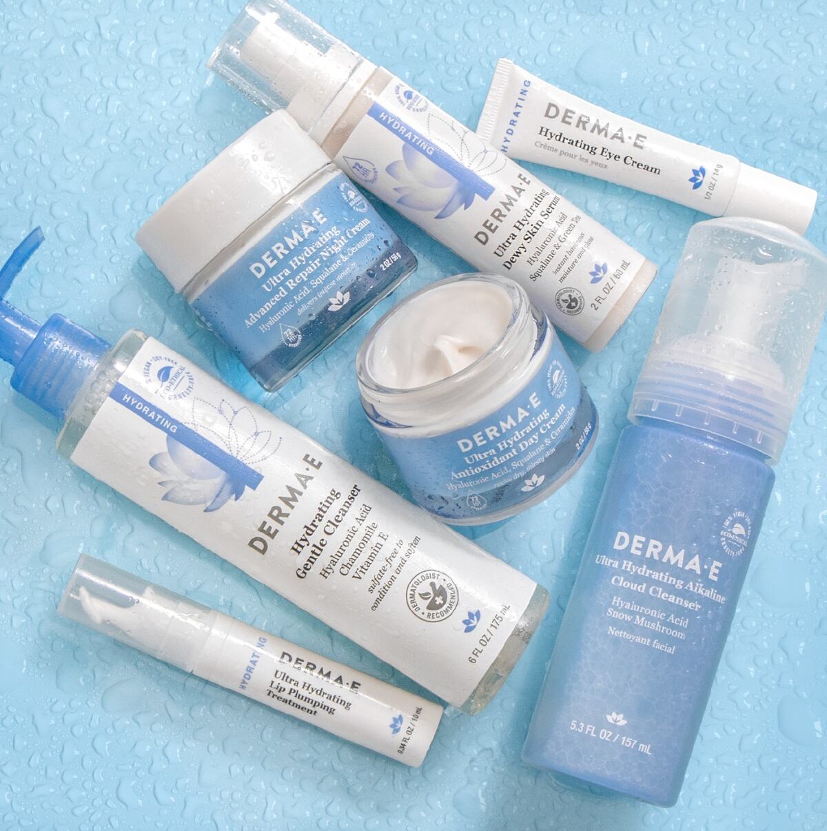 A collection of white and light blue bottles, tubes and jars of Derma-e skincare against a light blue background.