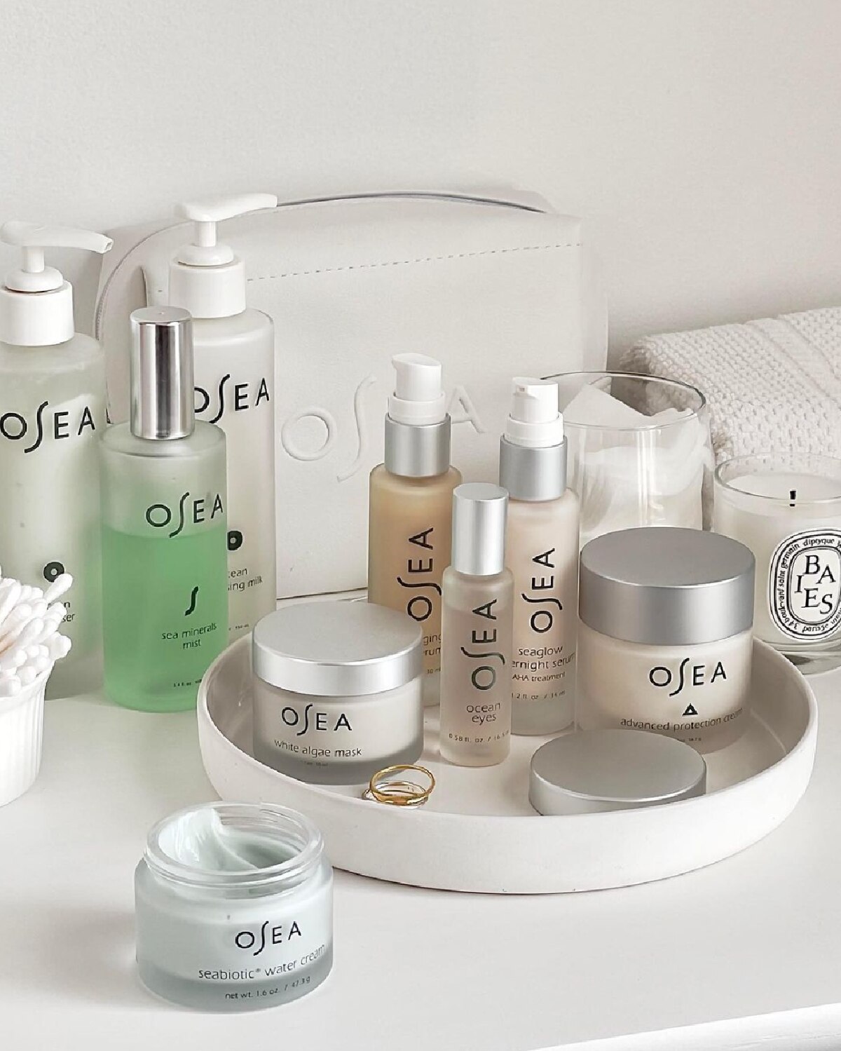 A white dish containing various Osea Malibu skincare bottles and jars against a white background with white toiletry bag. 