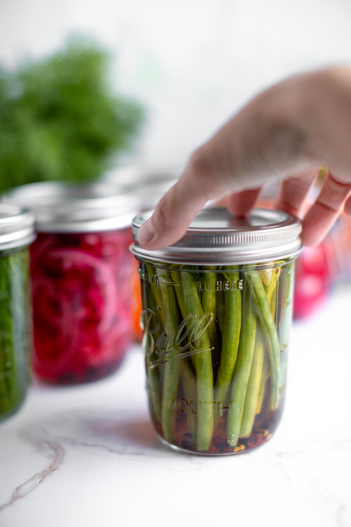 A hand reaching for a jar of quick pickled green beans.