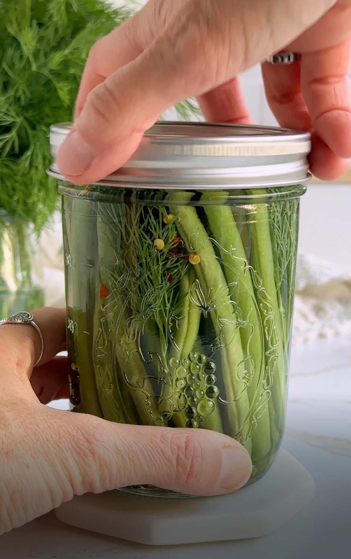 A lid being screwed onto a jar of pickled green beans.