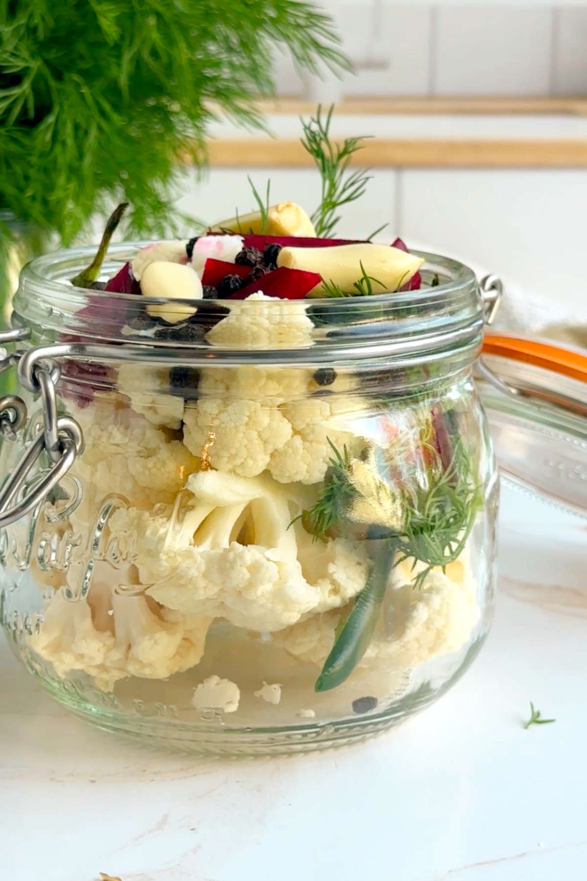 A glass just stuffed with the brim with cauliflower florets, beet chunks, garlic cloves, sliced habanero, and black peppercorns.