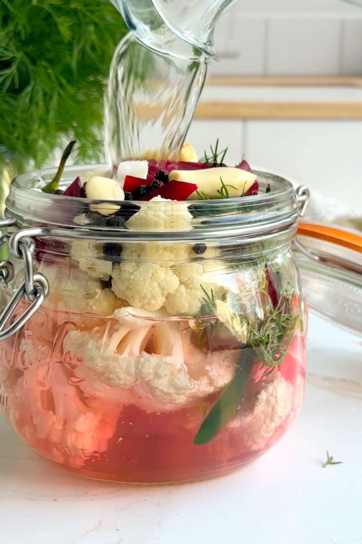 The pickling brine being poured over the jar of cauliflower florets and seasonings.