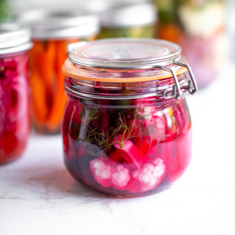 Pickled cauliflower in a glass jar with beets, dill, habanero slices, and garlic cloves.