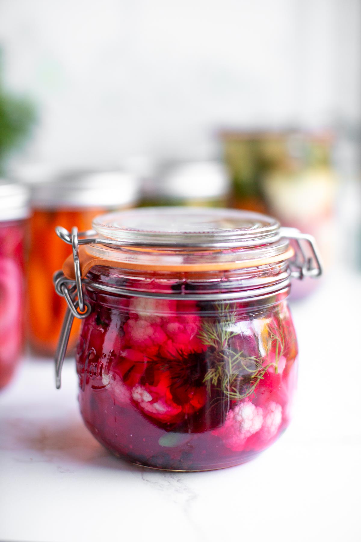 Quick pickled cauliflower in a glass jar with more pickled veggies in jars in the background.