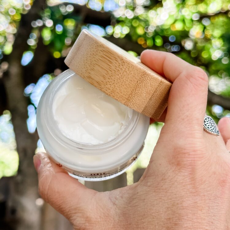 Woman holding a vegan face moisturizer in a glass container with a bamboo lid from Morrocco Method.