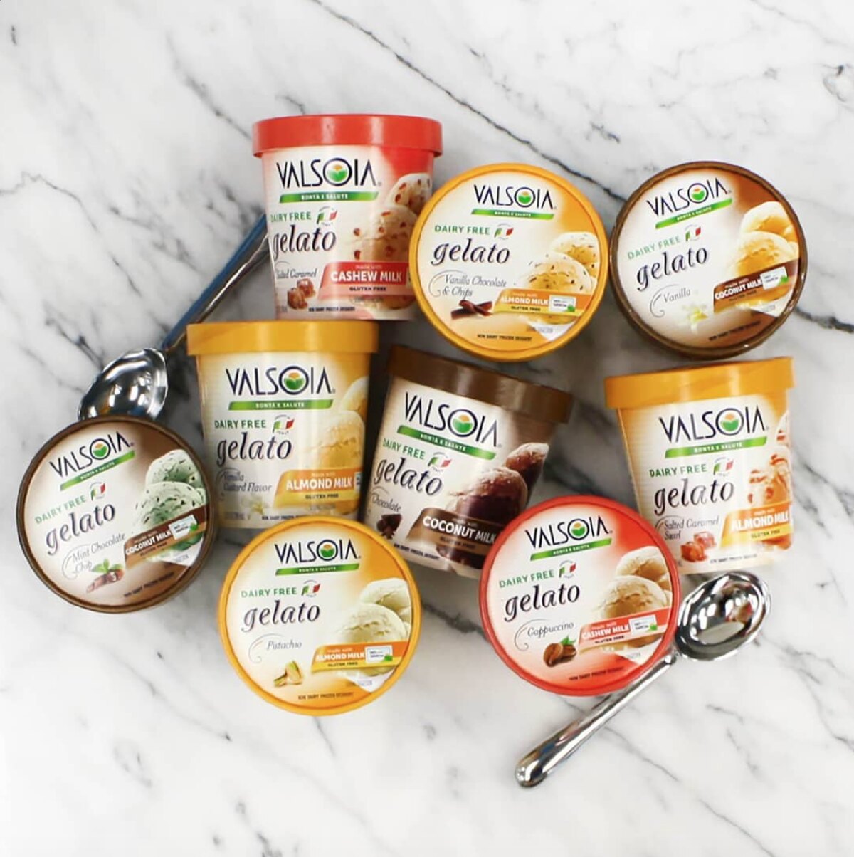 Nine pints of Valsoia dairy free gelato with spoons against a marble background. 