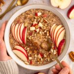 A bowl of apple cinnamon steel cut oats topped with apple slices and chopped nuts.