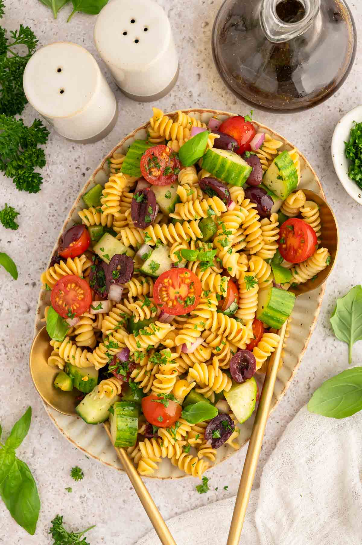 Vegan cold pasta salad on a serving platter with a serving spoon and fork.